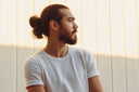 A man in a white tshirt with long hair up in a man bun,
