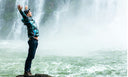 Man standing on a rock looking at a waterfall. Accomplished. Confident. Proud.