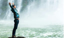 Man standing on a rock looking at a waterfall. Accomplished. Confident. Proud.