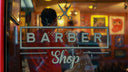 view through a barbershop window at night with barber shop lettering on the glass.