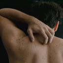 Man's back with his arm lifted up and on his neck.