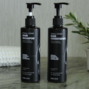 Two bottles of Tribal Chimp hair shampoo and conditioner on a marble surface with a plant in the background.