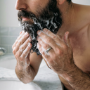 Man washing his beard with shampoo in a bathroom.