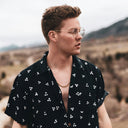 Man wearing a black patterned shirt with a scenic background