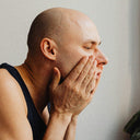 Man sitting in a bathroom with a counter full of items, looking distressed.