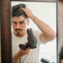 Man styling his hair with a hair dryer in front of a mirror.